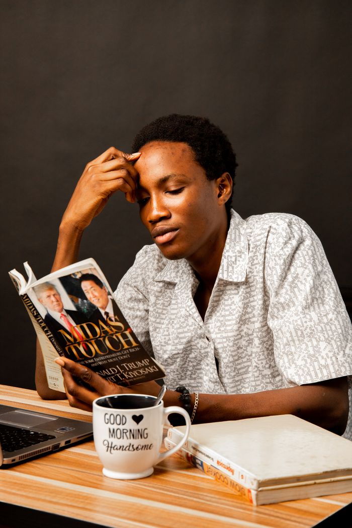 Young man reading 'Midas Touch' at a desk with a coffee mug. Relaxed and focused atmosphere.