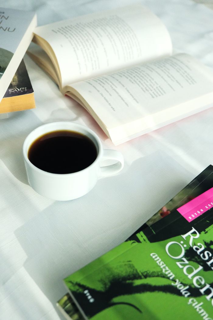 Cup of coffee beside open books on a white tablecloth.